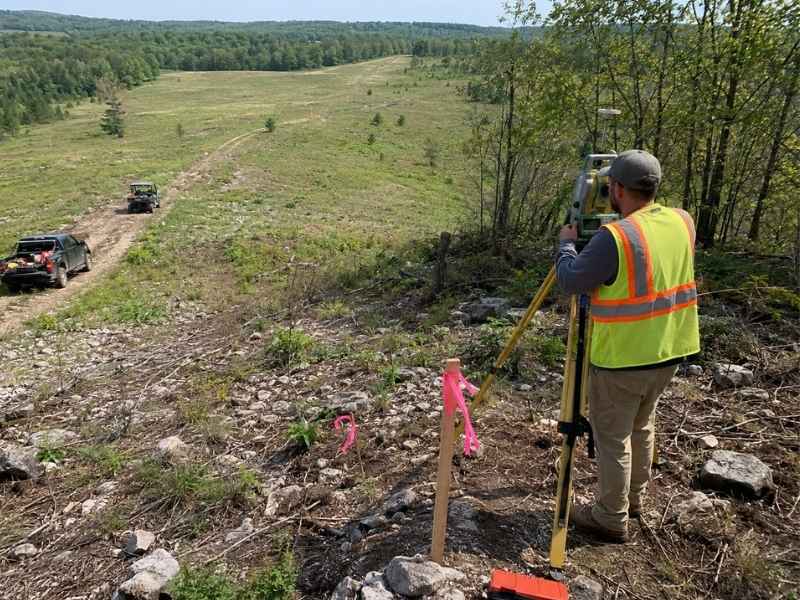 Boundary survey price chattanooga tennessee | Chattanooga Land Surveying Surveyor in a high-visibility vest uses surveying equipment on a rocky hillside, with two off-road vehicles on a dirt road in the background.